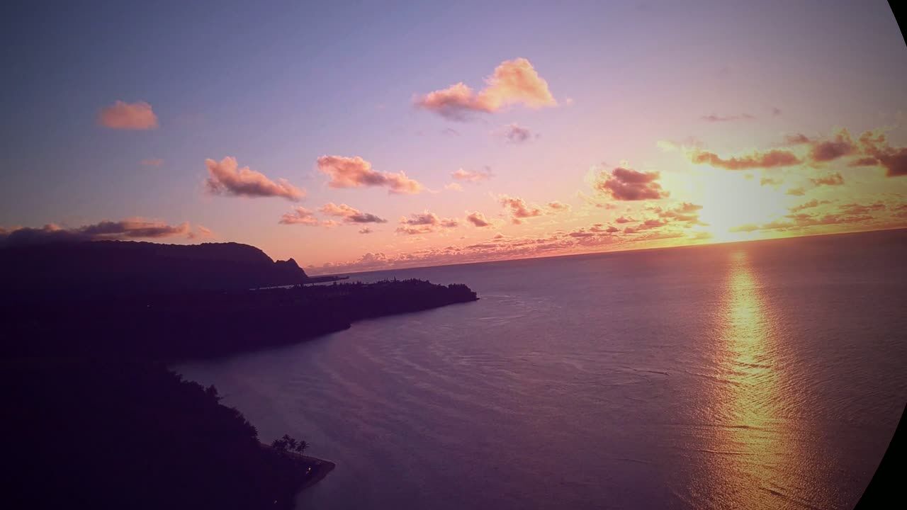 Pink and gold dusk over a dark headland and calm bay